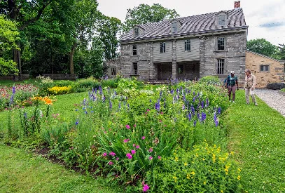 Colorful flower garden in front of the historic stone farmhouse at Bartram's Garden, with two visitors on the lawn