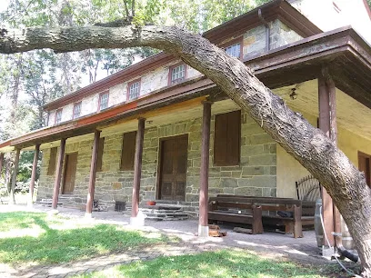 Old stone Darby Friends Meeting House with a wooden porch and a large tree trunk leaning across the front