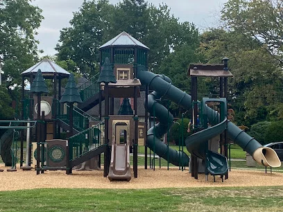 Playground at Glenolden Park with wooden towers, green tube slides and mulch ground, surrounded by trees