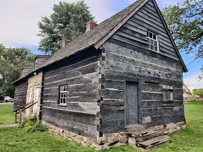 Weathered log house with a shingled roof, brick chimneys and stone foundation at Morton Homestead in Prospect Park, PA