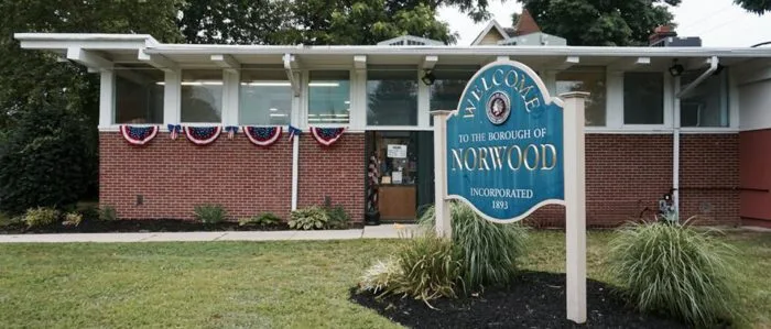 Welcome to the Borough of Norwood sign in front of a brick building with patriotic bunting, Norwood Public Library