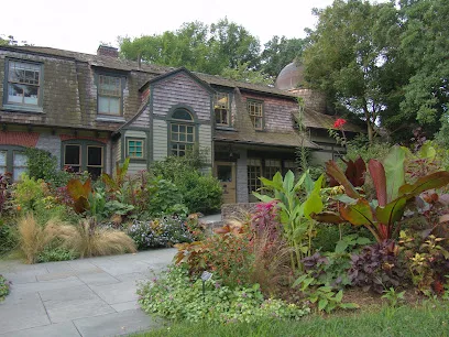 Colorful flower garden with tropical foliage in front of a shingled stone building at Scott Arboretum, Swarthmore